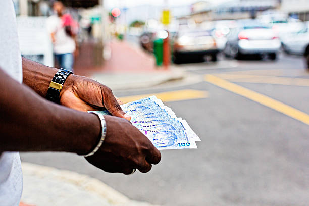 istockphoto-174973009-612x612 A man stands on a street corner holding a bundle of the new South African One Hundred Rand notes featuring the iconic statesman Nelson Mandela .